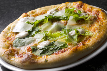 Caesar pizza on a white plate on a black marble