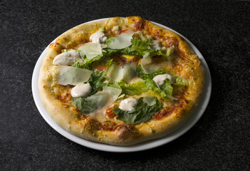 Caesar pizza on a white plate on a black marble