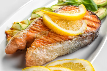 Delicious roasted salmon steak with slices of lemon and vegetable on plate, closeup