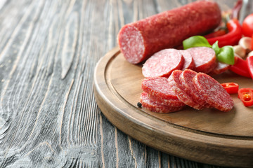 Wooden board with delicious sliced sausage and chili pepper on table
