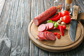Wooden board with delicious sliced sausage and chili pepper on table