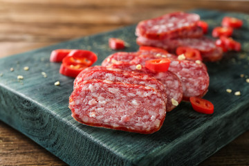 Wooden board with delicious sliced sausage and chili pepper on table