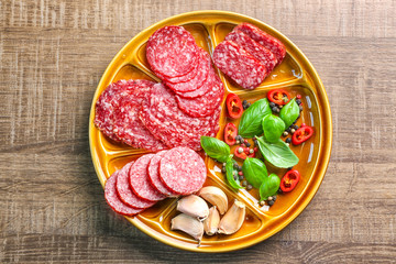 Plate with sliced different sausages and chili pepper on table