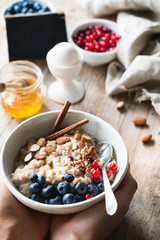 Oatmeal porridge bowl with superfoods in hands. Hands holding bowl of oat porridge with blueberries, almonds, linseed, cinnamon and currants. Selective focus