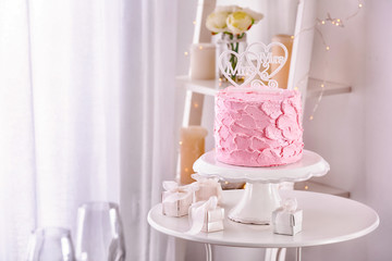 Stand with delicious cake for lesbian wedding and gifts on table