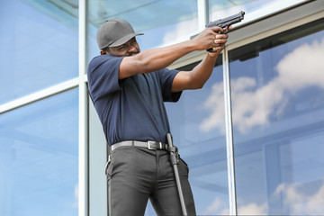 Male security guard taking aim near big modern building