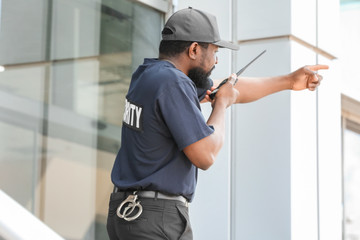 Fototapeta na wymiar Male security guard using portable radio transmitter near big modern building