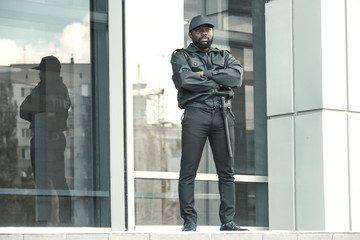 Male security guard standing near big modern building - obrazy, fototapety, plakaty