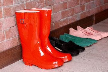 Red wellington boots and different shoes on floor near wall