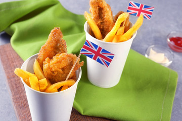 Paper cups with English traditional fish and chips on table