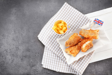 Wooden board with tasty fried fish and chips on table