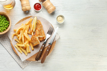 Fried fish and chips with peas on white wooden background