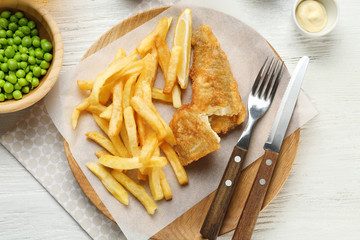 Fried fish and chips with peas on white wooden background