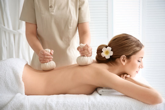 Beautiful young woman having back massage with herbal bags
