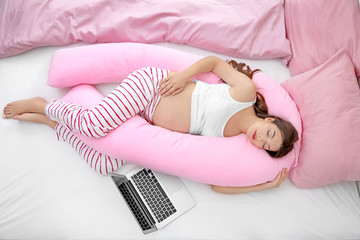 Young pregnant woman sleeping on maternity pillow in bed