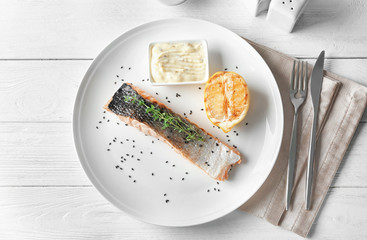 Plate with slice of delicious salmon and fish sauce on table