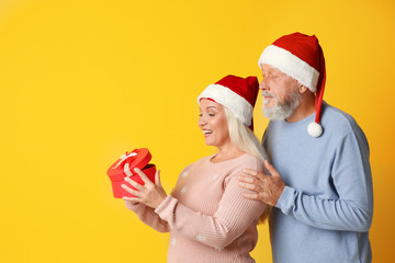 Obraz premium Happy senior couple with Christmas gift on color background