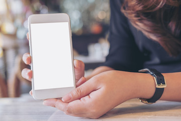 Mockup image of a woman holding and showing white mobile phone with blank screen on the table in modern cafe