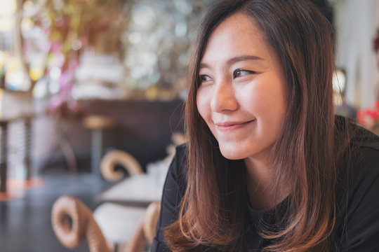 Closeup portrait image of a smiley beautiful Asian woman with feeling good sitting and relaxing in modern cafe
