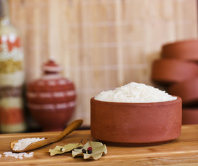 White rice in a clay bowl and in a wooden spoon. Bay leaves and black peppercorns.
