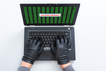 Computer Criminal in Gloves working on Laptop Access Denied sign