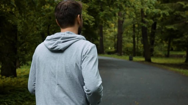 Young powerfull handsome runner outside in autumn nature park jogging with iphone. Super slow motion shot with steadicam. Back spine middle view