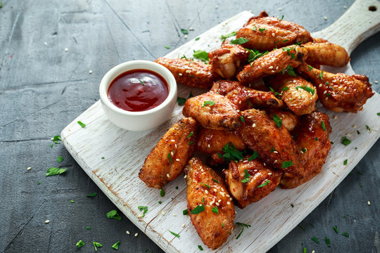 Baked chicken wings with sesame seeds and sweet chili sauce on white wooden board.