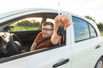 Happy young smiling man sitting inside new car with keys.