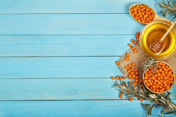 Berries of sea-buckthorn in a bowl with honey on a blue wooden background with copy space for your text. Top view