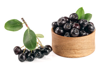 Chokeberry with leaf in wooden bowl isolated on white background. Black aronia berries