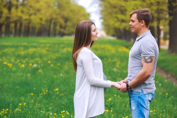 Obraz premium Pregnant woman with husband walking and holding hands in park