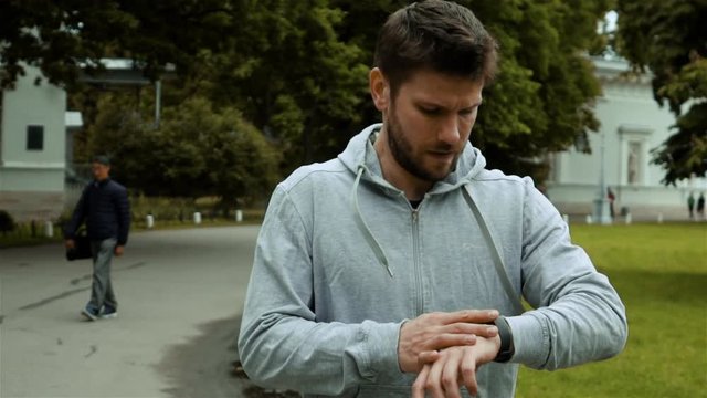 Runner at Autumn Park Checks Fitness Results Sport Tracker Wristband Watch. Slow motion front shot.