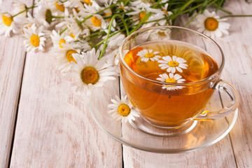 Herbal tea with fresh chamomile flowers on white wooden background