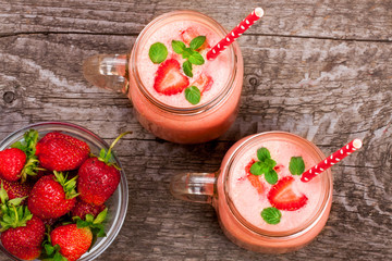 Glass of strawberry yogurt or smoothie with mint leaves on old wooden background. Top view