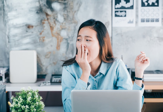 Young Asian Casual Businesswoman Yawn In Front Of Laptop Computer And Looking Through Office Window With Bored Feeling ,hard Work Concept.