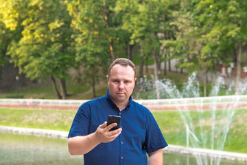 Man in blue shirt uses his smart phone on nature background