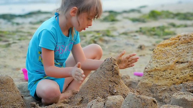 Close-up a six-year girl builds a sand castle on the beach on the sea coast.