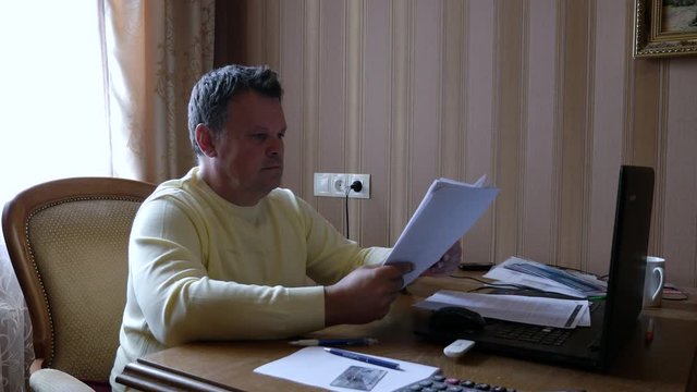 Angry businessman scatters documents on the desk at work in home office.