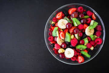 Natural breakfast, fruit salad in glass plate on black table. Flat lay, top view