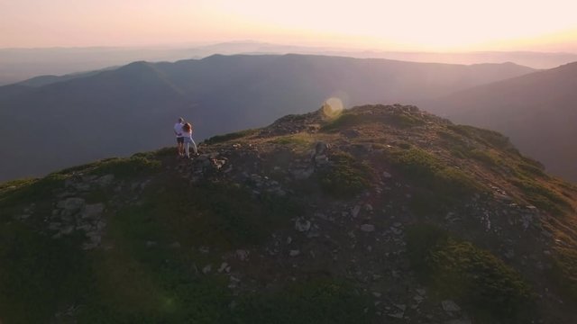 Video of drone flying over couple of hikers or tourists, man and woman, adventurers or climbers overlooking and enjoying sunset over high smokey mountains, inspiring and romantic love dream