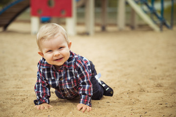 Happy little baby boy playing on the playground in the summer or autumn day