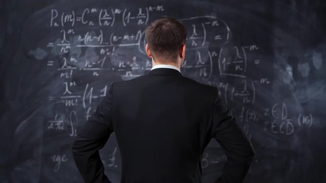 Rear view of man against chalkboard with math formula equations. He think about solution and try to understand high university task.