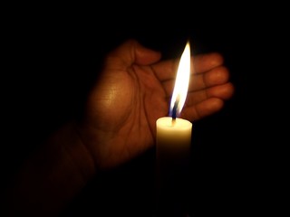 Hand covering flame of candle from wind