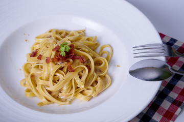 Spaghetti . Fettuccine carbonara in a white bowl, garnished with bacon, mushrooms. Delicious creamy sauce, with white background and silverware