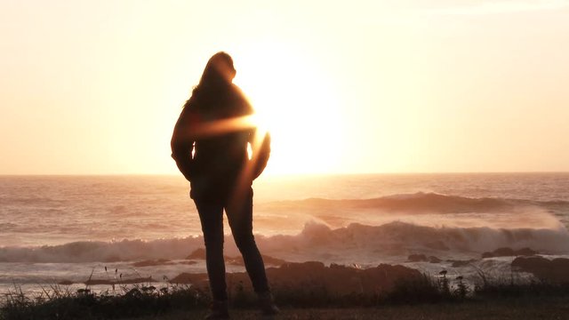 Slow motion of model released woman standing on coastline watching the sun go down on beautiful evening in Oregon.