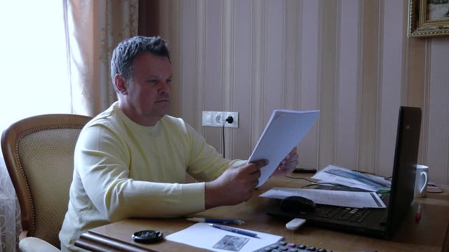 Angry businessman scatters documents on the desk at work in home office.