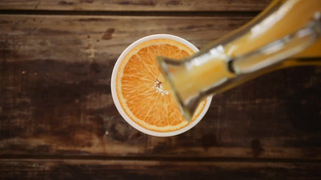 Endless loop of organic orange juice being poured into a glass that stands on wooden table in cafe, bar or restaurant, serving refreshing summer beverage made from fruits