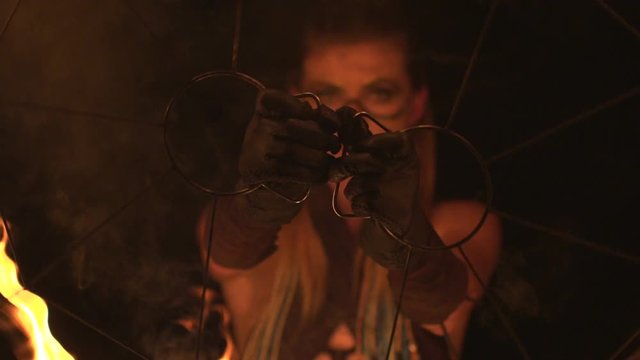 Young girl with beautiful eyes dances with burning torches made in shape of fans at fire show.