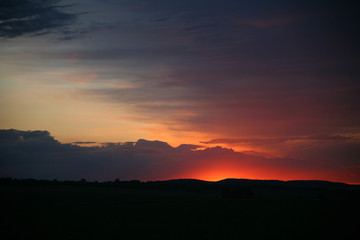Natural Sunset Sunrise Over Field Or Meadow. Bright Dramatic Sky And Dark Ground. Countryside Landscape Under Scenic Colorful Sky At Sunset Dawn Sunrise. Sun Over Skyline, Horizon. Warm Colours.