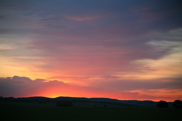 Natural Sunset Sunrise Over Field Or Meadow. Bright Dramatic Sky And Dark Ground. Countryside Landscape Under Scenic Colorful Sky At Sunset Dawn Sunrise. Sun Over Skyline, Horizon. Warm Colours.